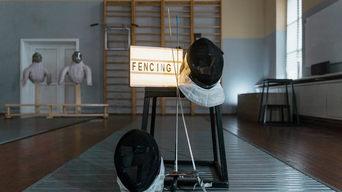 Fencing gear including masks and swords displayed in a training room.